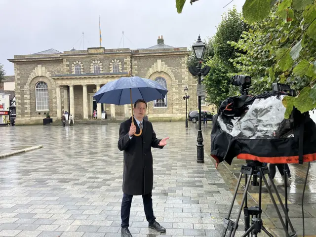 Duncan Kennedy stands in front of a camera whilst holding an umbrella