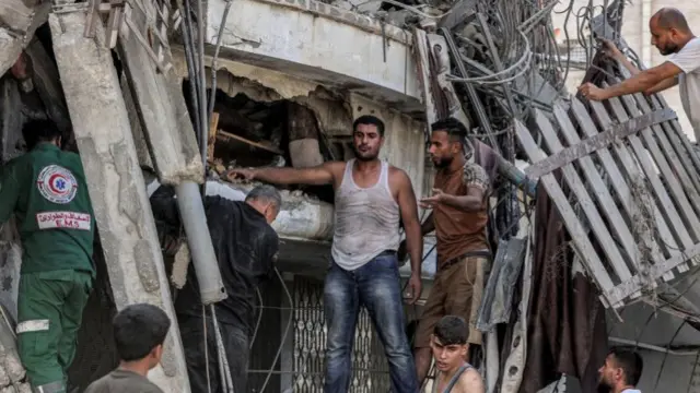 Men gather around a whole in a collapsed building, seeking to rescue someone inside