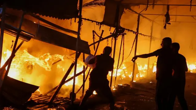 People throw buckets of water at an enormous fire raging through a tent camp