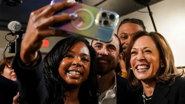 Kamala Harris, smiling, takes a selfie with a woman and two men in an art gallery