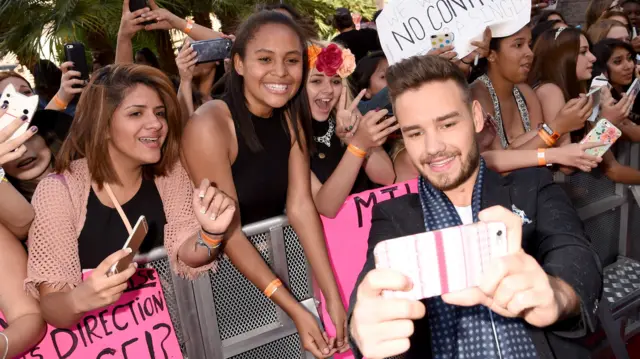 Liam Payne poses for a selfie next to a selection of fans who beam and smile. they stand in front of a gate