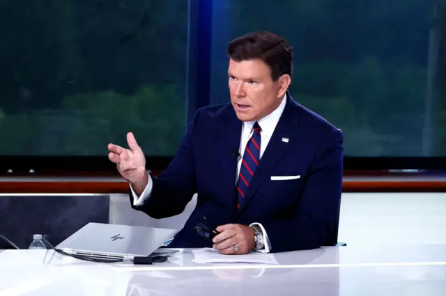 Bret Baier, in a blue suit and striped tie, gestures during his show