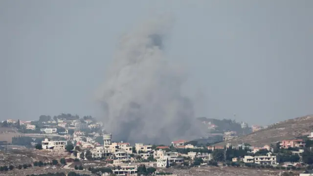 A large plume of smoke rises amid a collection of buildings