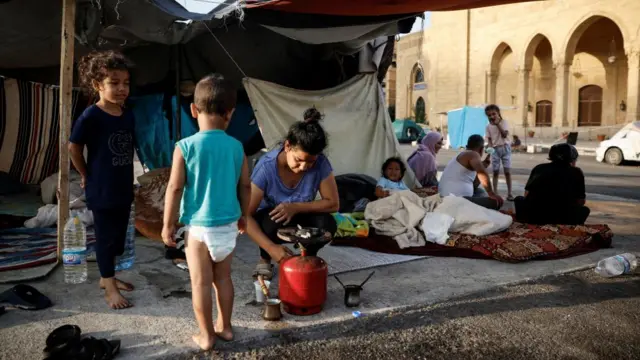 A woman makes coffee on the streets of central Beirut while young children stand near her.