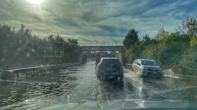 Cars proceed through shallow water on a main road