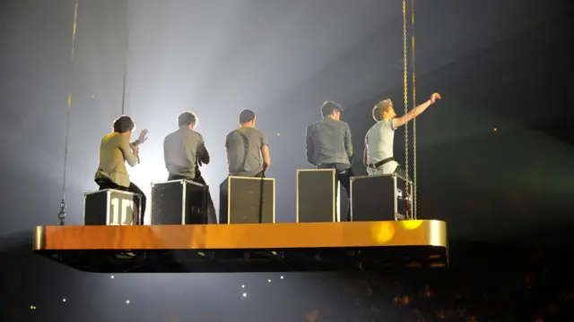 The members of One Direction sit on an elevated platform during a performance