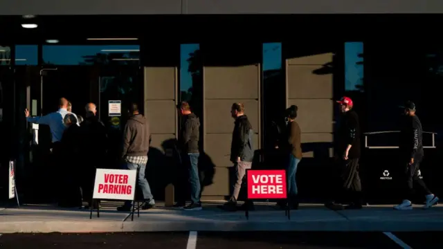 A queue of people stand in line outside a grey building in Wilmington, North Carolina