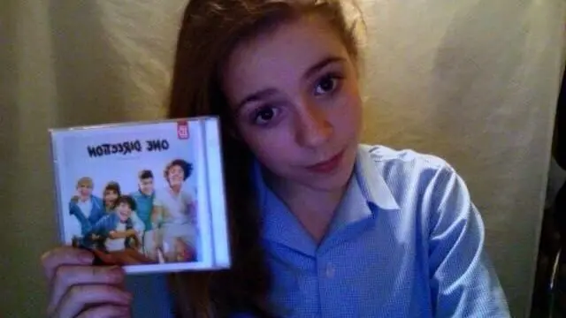 Kitty Williams holds up a One Direction album. she sits in front of a white sheet and wears a blue shirt.