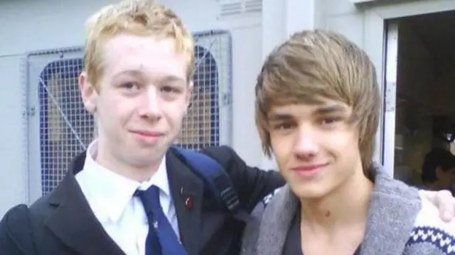 Photo of a young John Payne standing in his school uniforrm with his arm around Liam Payne who is wearing a grey cardigan, both boys are smiling