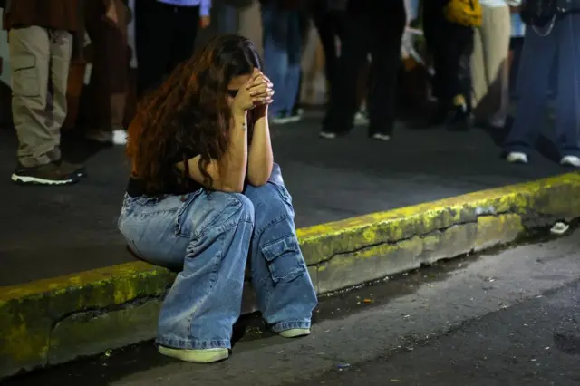 A woman sits on the curb with her head in her hands