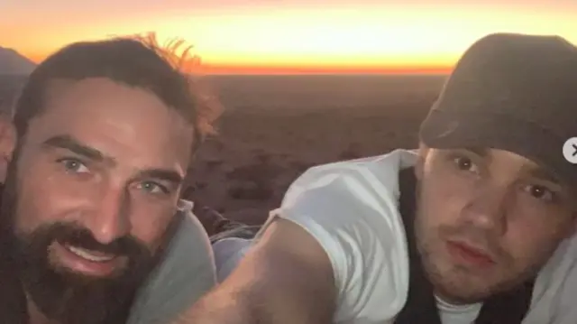 Ant Middleton and Liam Payne laying down with a sunset and deserted ground behind them