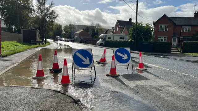 A flooded road with traffic signs out to warn motorists