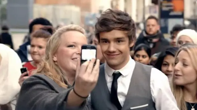 Jo Shatford poses with Liam Payne in the music video for One Thing by One Direction. They are standing in front of a group of mostly women on busy London street