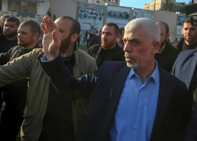 Hamas leader Yahya Sinwar at a rally in Gaza in April 2023, waving his hand and a group of bystanders behind him