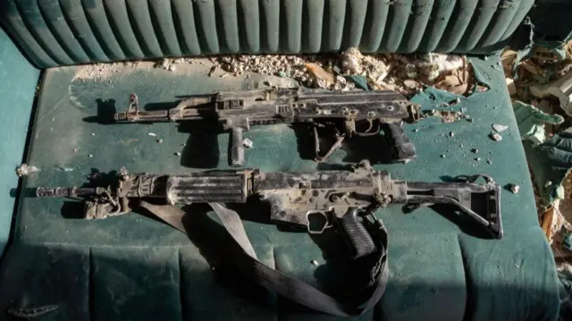 Two machine guns laying on what appears to be a forest green velvet couch covered in dust and debris