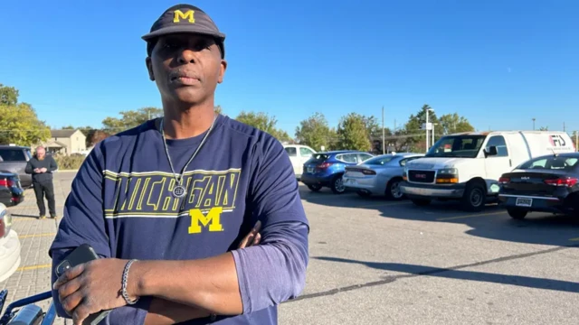 Darrell Sumpter standing in a parking lot with his arms crossed looking at the camera holding his phone in one hand