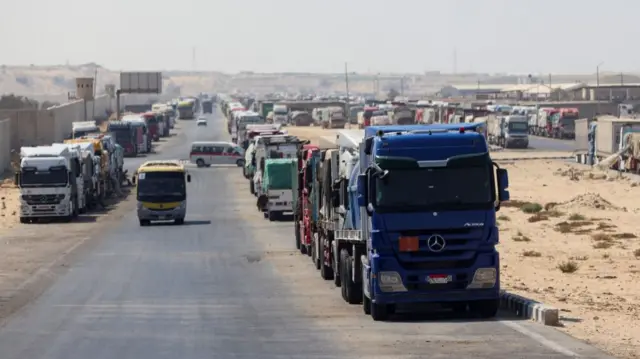 rows of lorries carrying humanitarian aid lined up at sides of street waiting to be allowed into Gaza