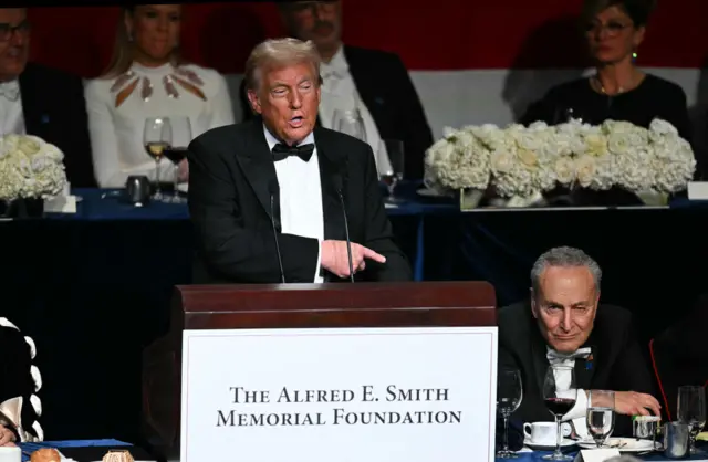 Donald Trump give a speech in front of a podium that has the words "The Alfred E Smith Memorial Foundation" on a sign in front of it