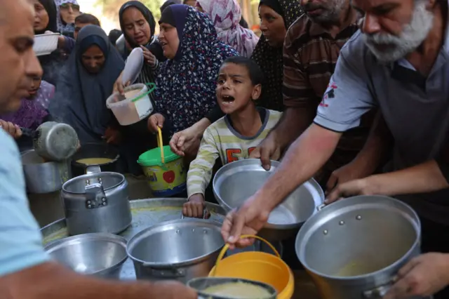 Group of people - including a young child - carrying pots, crowd around as a man distributes food rations in northern Gaza