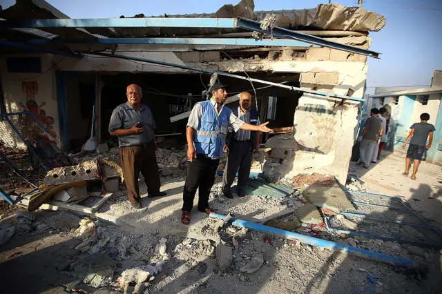 Men stand at the site of the  Abu Hussein School hit by a Israeli tank shell attack