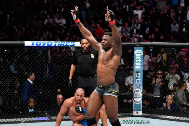 Francis Ngannou celebrates with Ciryl Gane on the canvas behind