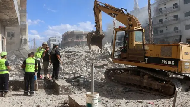 Several rescuers look on as an excavator digs to reach victims through the rubble of a building in southern Lebanon.