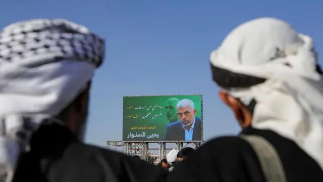 People stand in front of the billboard showing late Hamas leader Yahya Sinwar as protesters, mainly Houthi supporters, rally to show support to Lebanon's Hezbollah and Palestinians in the Gaza Strip, in Sanaa, Yemen October 18, 2024