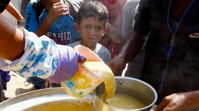 A child looks on as Palestinians gather to receive food cooked by a charity kitchen, amid the Israel-Hamas conflict, in Khan Younis in the southern Gaza Strip, October 16, 2024.