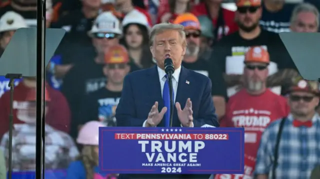 Trump speaking to the crowd from behind bulletproof glass