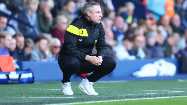 A kneeling Millwall manager Neil Harris