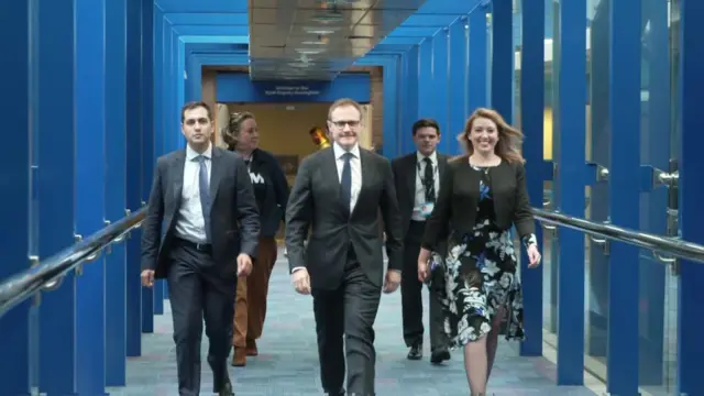 Tom Tugendhat walking through a corridor with four people to his side