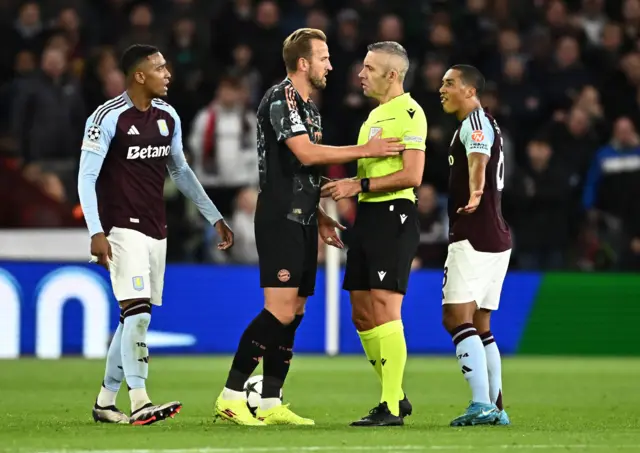 Kane talks to the referee while Konsa looks on