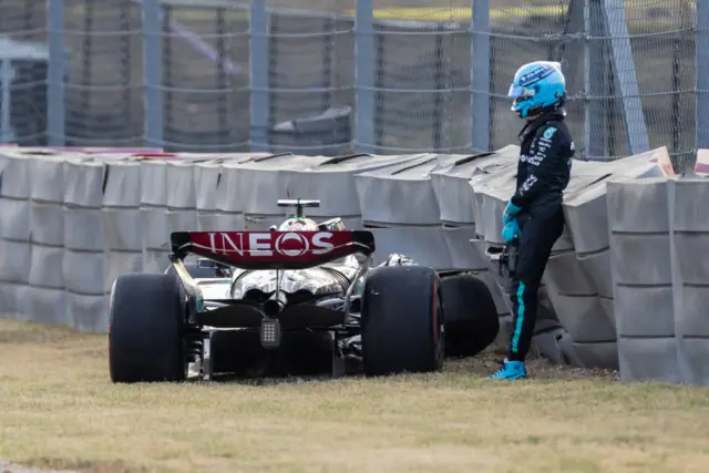 George Russell stands next to his car after crashing