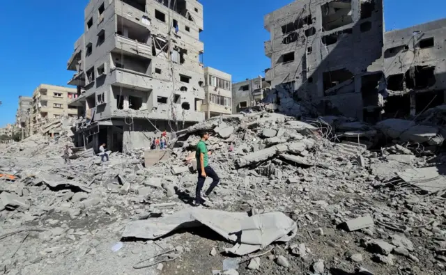 A man walks past a large pile of rubble surrounded by severely damaged buildings in the Beit Lahia, northern Gaza