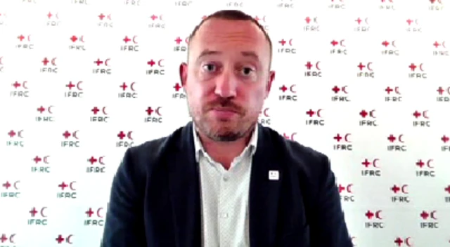 Tomasso Della Longa, a spokesperson for the International Federation of Red Cross and Red Crescent Societies, sitting in front of a bannered background