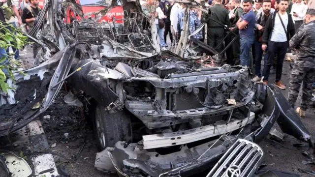 A crowd of people crowding around a car which was attacked in Syria.