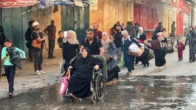 Line of Palestinians holding their belongings as they leave Beit Lahia in northern Gaza following Israeli evacuation orders, with a woman being pushed in a wheelchair at the front