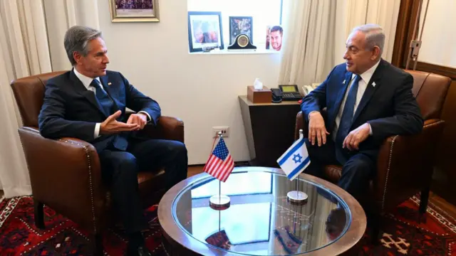 Blinken and Netanyahu sat either side of a small glass coffee table with small USA and Israel flags on the table. Both men are wearing dark suits