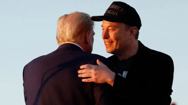 Trump and Musk embrace, with Musk wearing a "Make America Great Again" hat