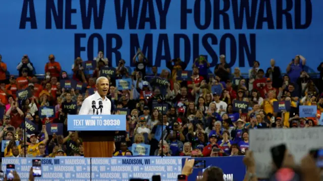 Barack Obama stands at a stage in Madison, Wisconsin with the words A new way forward for Madison emblazoned on the back wall