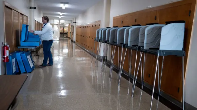 A man setting up a voting station, with voting booths lined up in a hallway