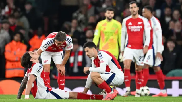 Riccardo Calafiori of Arsenal down with an injury as Leandro Trossard and Kai Havertz of Arsenal check on him