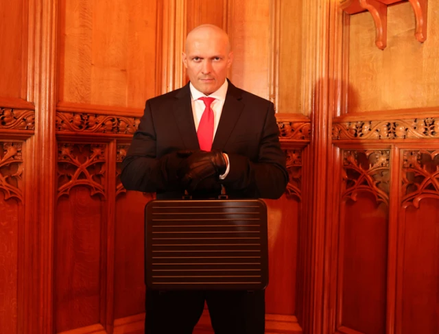 Oleksandr Usyk with a briefcase dressed in a black suit and red tie