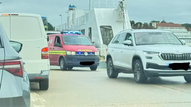 A red fire and rescue van with a white 4x4 car in front getting off a ferry ramp