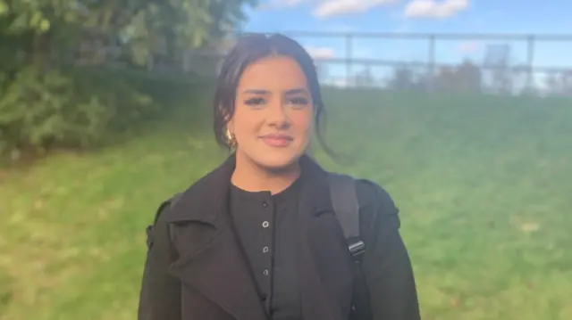 A woman in a black top and coat near some grass