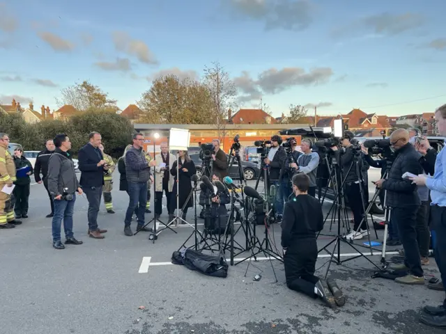 Members of the press gather in a car park