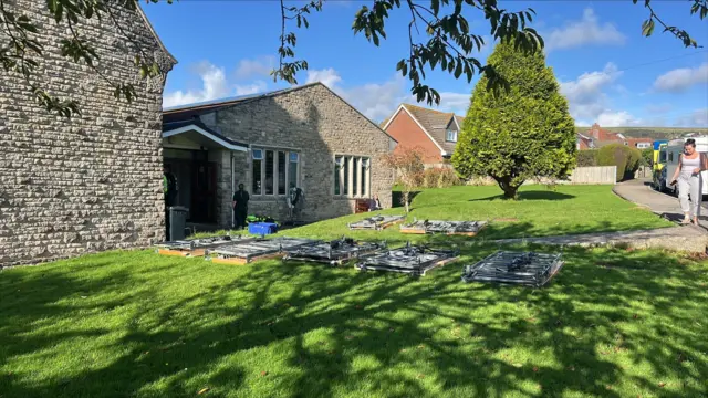 The outside of a pale beige brick church with greenery and beds laid down on the grass