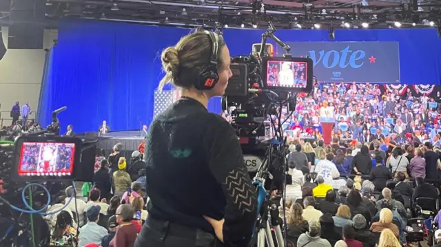 A woman operating a camera behind a large crowd of people