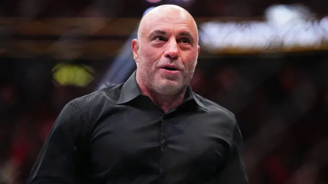 Joe Rogan, wearing a black dress shirt, reacts during UFC 300 in Las Vegas, Nevada