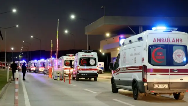 A line of ambulances, at least seven, most with their lights flashing